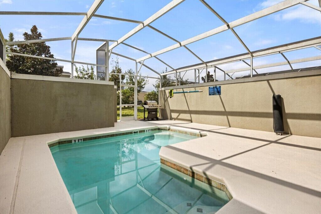 A covered swimming pool with a clear roof structure, a concrete wall, and a blue sign on the wall.