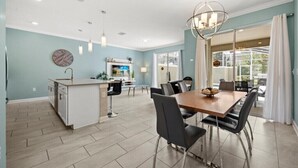 A modern kitchen with a central island, dining area with chairs, and a large window with curtains. - Last Minute Disney Getaway! Private Pool & Themed Bedrooms. Book Now! #161419 (Orlando)