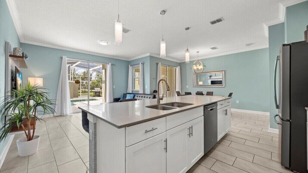 A modern kitchen with a large island, white cabinetry, and a black refrigerator. - Last Minute Disney Getaway! Private Pool & Themed Bedrooms. Book Now! #161419 (Orlando)