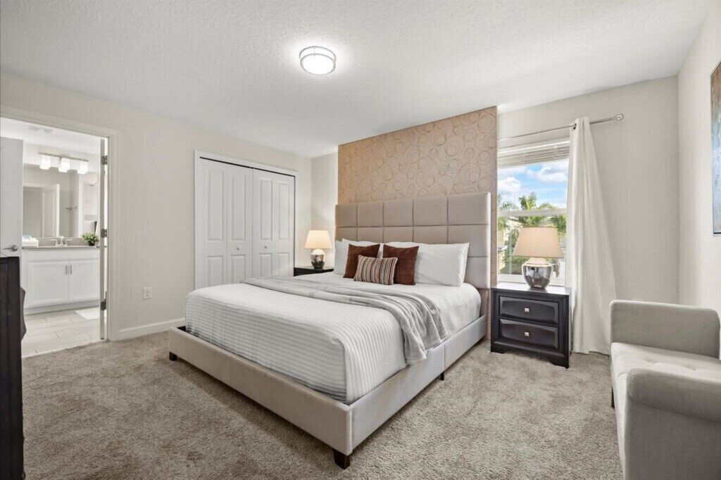 A bedroom with a large bed, a nightstand with a lamp, a dresser, and a window with curtains.