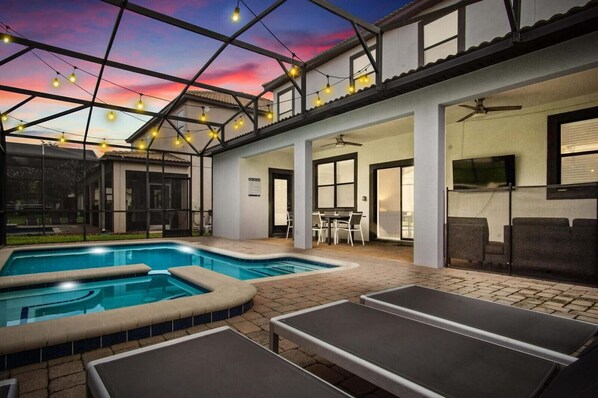 Un área de piscina exterior moderna con techo de vidrio, una zona de comedor y una pantalla de televisión.