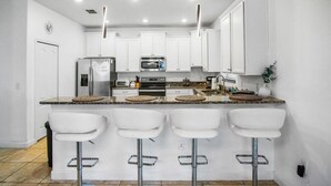 A modern kitchen with white cabinets, stainless steel appliances, and a bar area with white stools. - Last Minute Disney Getaway! Private Pool, Game Room & Themed Bedrooms. Book Now! #162951 (Orlando)
