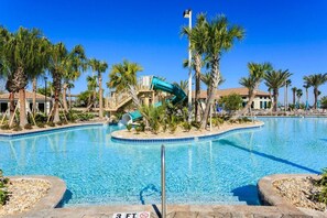Una piscina con tobogán de agua, palmeras y un cielo azul despejado.