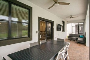 Un espacio moderno para comer al aire libre con mesa y sillas, un sofá y ventiladores de techo.