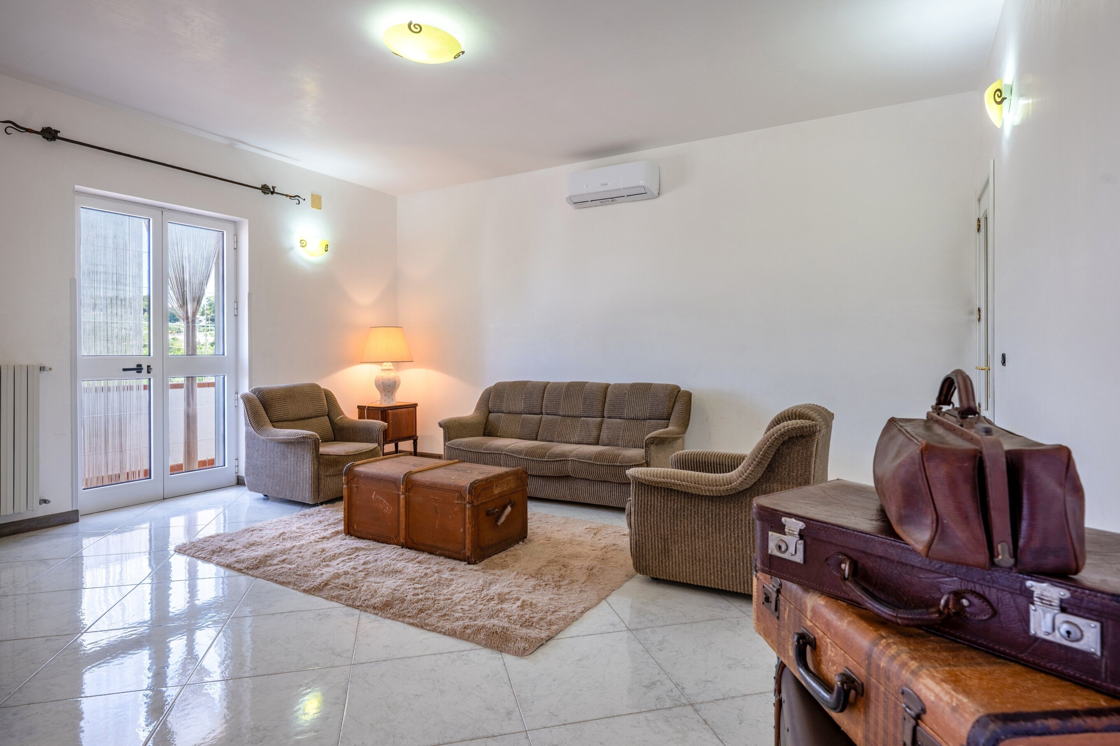 A living room with a sofa, armchairs, a lamp, a fireplace, and a suitcase.