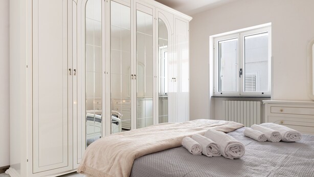 Een slaapkamer met een bed, een kledingkast, een raam en een radiator.