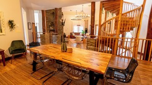 En rummelig spiseafdeling med et langt træbord, moderne stole og en trappe til et højere niveau.