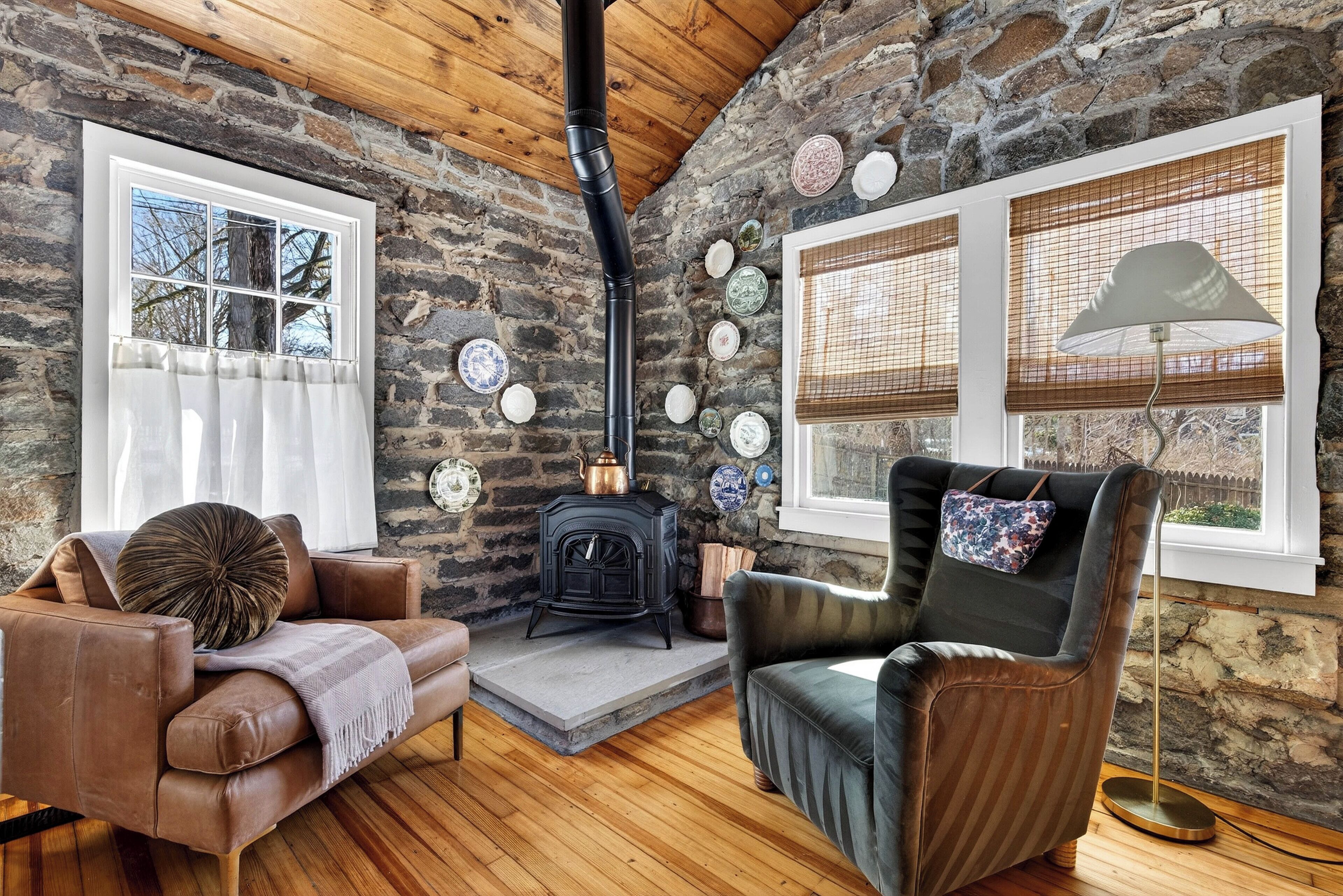 A cozy room with a stone wall, a fireplace, a sofa, a chair, and a lamp.