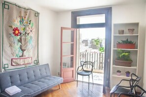 A cozy living room with a grey sofa, a chair, a bookshelf with plants, and a large window with a view of the city. - Location, bright, spacious, quiet and quiet (Buenos Aires)