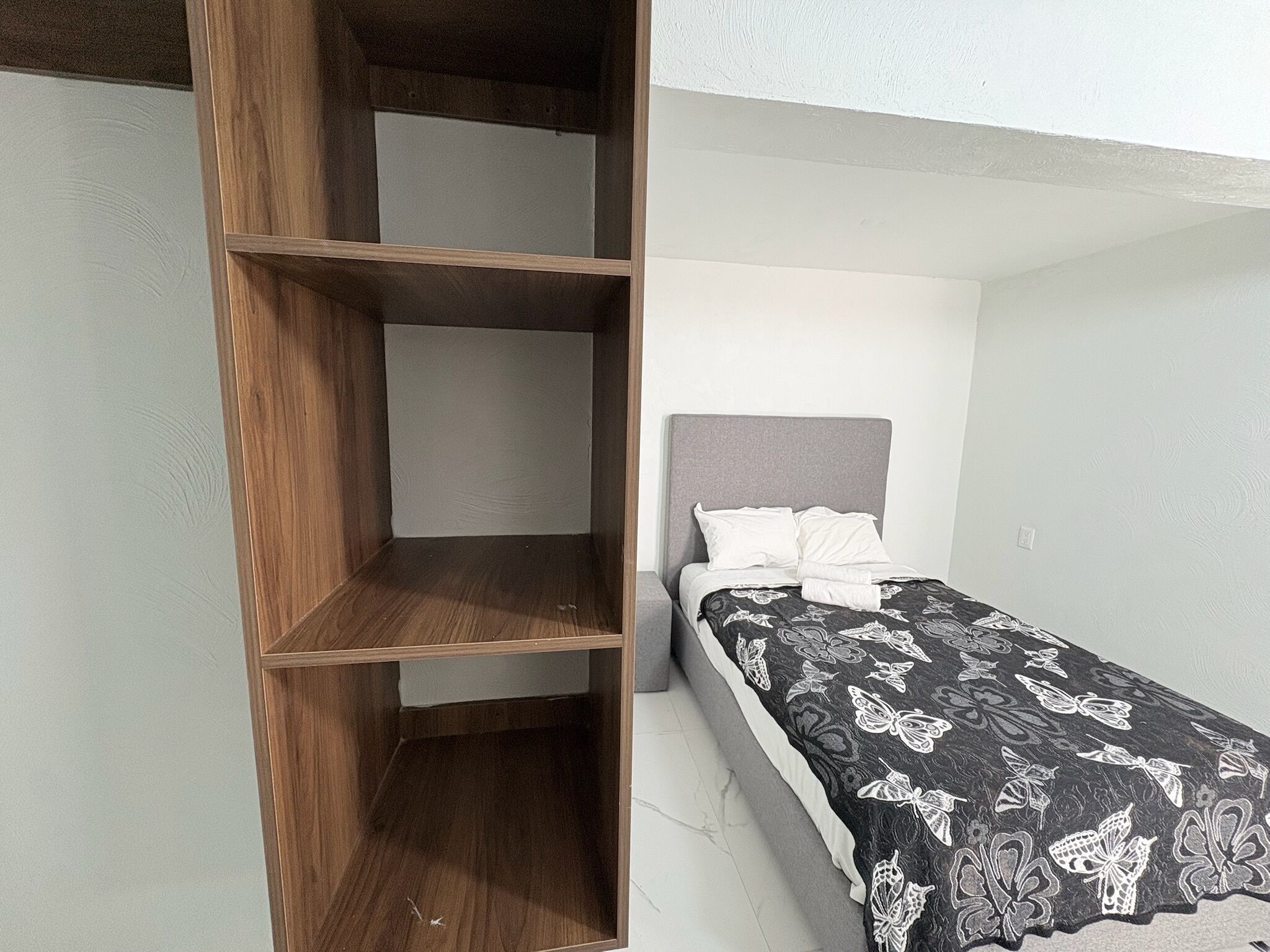 A bedroom with a bed, a wooden wardrobe, and a white wall.