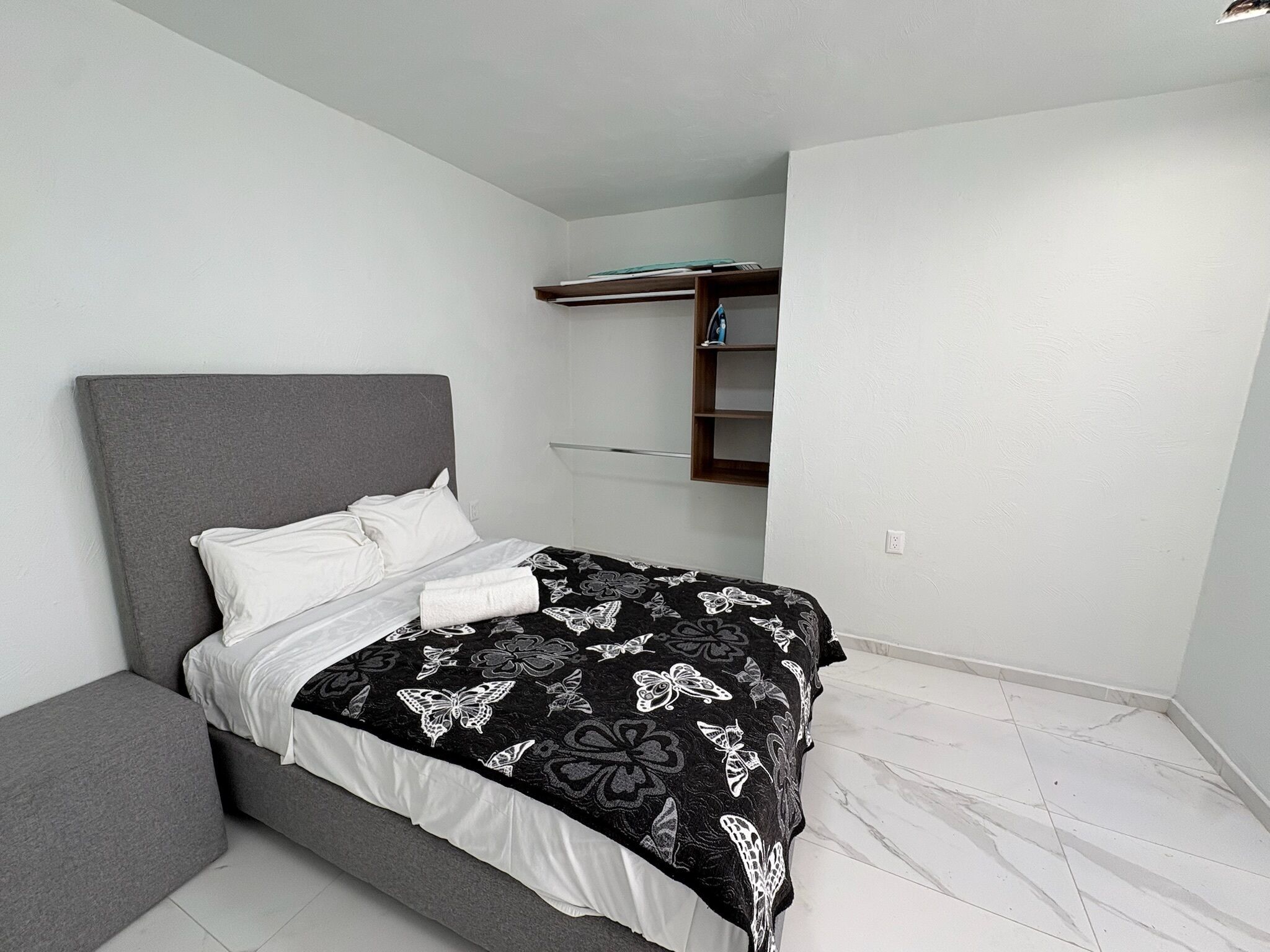 A bedroom with a grey headboard, a black and white patterned bedspread, a white pillow, and a neatly made bed.