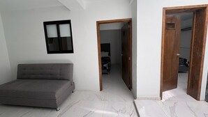 A room with a grey sofa, a wooden door, and a tiled floor. - Departamento Residencial San Juan Bosco  (Guadalajara)