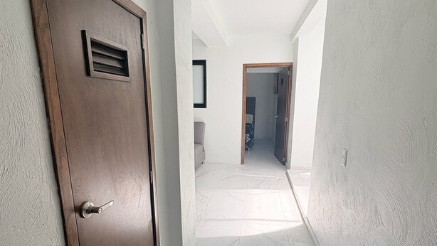 A hallway with a wooden door, white walls, and a tiled floor. - Departamento Residencial San Juan Bosco  (Guadalajara)
