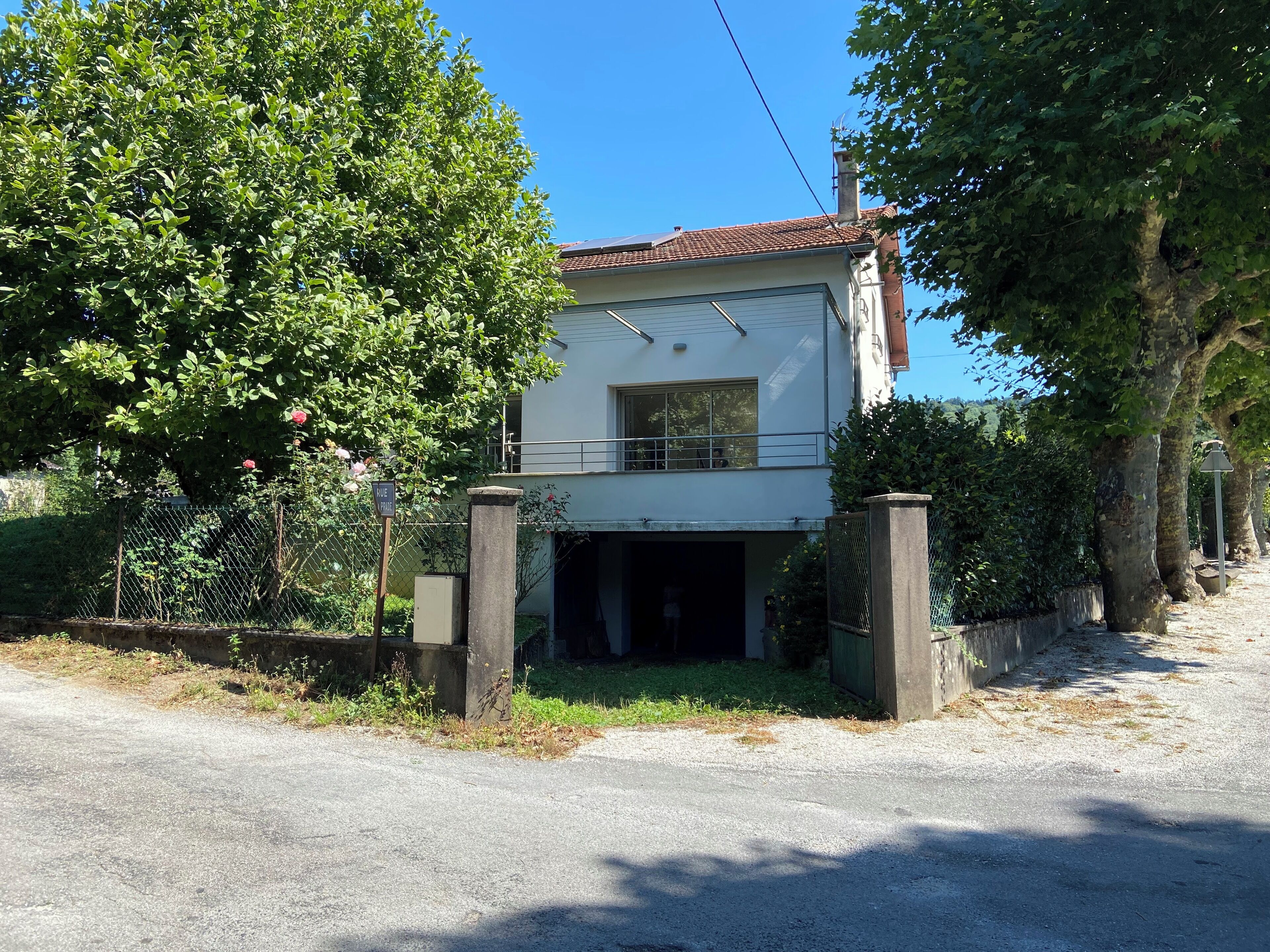 Een twee verdiepingen tellend huis met een garage, omgeven door bomen en een hek.