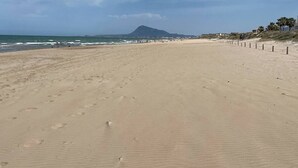 A wide sandy beach with footprints, a distant mountain, and a clear sky. - Balcony overlooking the Mediterranean Sea, wonderful natural fine sandy beach (Oliva)