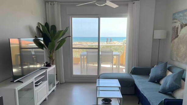 A modern living room with a television, a sofa, a coffee table, and a balcony with a view of the sea. - Balcony overlooking the Mediterranean Sea, wonderful natural fine sandy beach (Oliva)