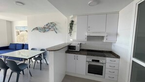 A modern kitchen with white cabinets, a microwave, an oven, and a dining area with a table and chairs. - Balcony overlooking the Mediterranean Sea, wonderful natural fine sandy beach (Oliva)