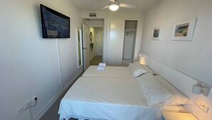 A hotel room with a large bed, a ceiling fan, a TV mounted on the wall, and a door leading to a hallway. - Balcony overlooking the Mediterranean Sea, wonderful natural fine sandy beach (Oliva)