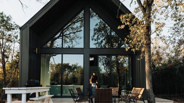 A modern building with large windows and a deck area with outdoor furniture.