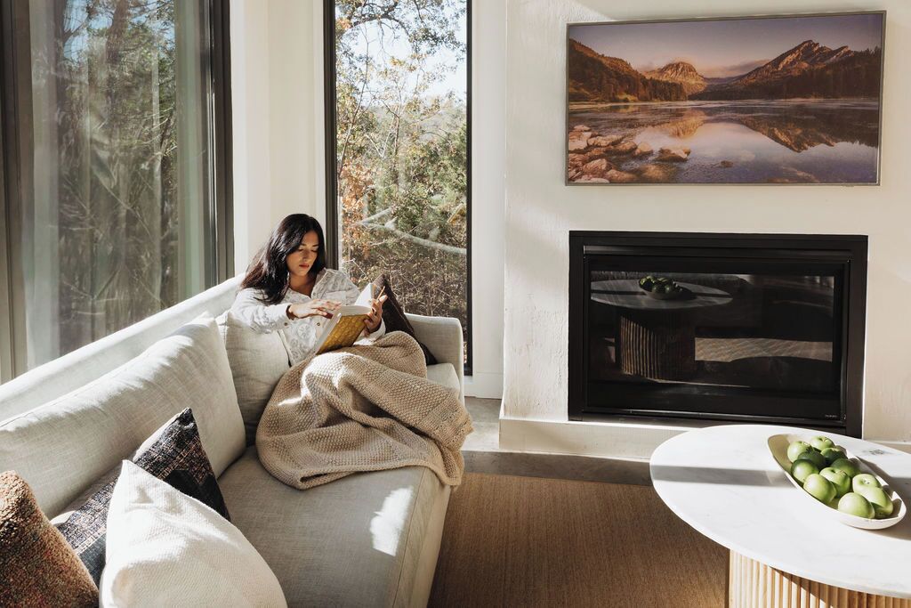 A modern living room with a large window, a fireplace, and a painting of a mountain landscape.