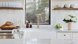 A modern kitchen with a large window, white cabinetry, and a marble countertop.