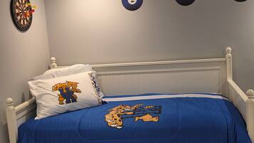 Un dormitorio con cama, un almohadón con personaje de caricatura, una colcha azul, un dardo y una mesa de billar con bolas numeradas.