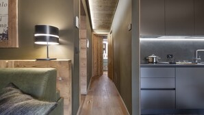 Ein schmaler Flur mit Holzboden, einem grünen Sofa, einer Lampe und einer Küchenzeile mit Spüle und Schränken.