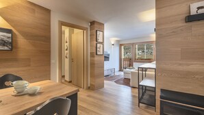 A modern interior with wooden flooring, a dining area with a table and chairs, and a view of the outdoors through large windows. - AlpinWood - Two Bedroom Apartment, Sleeps 5 (Temù)