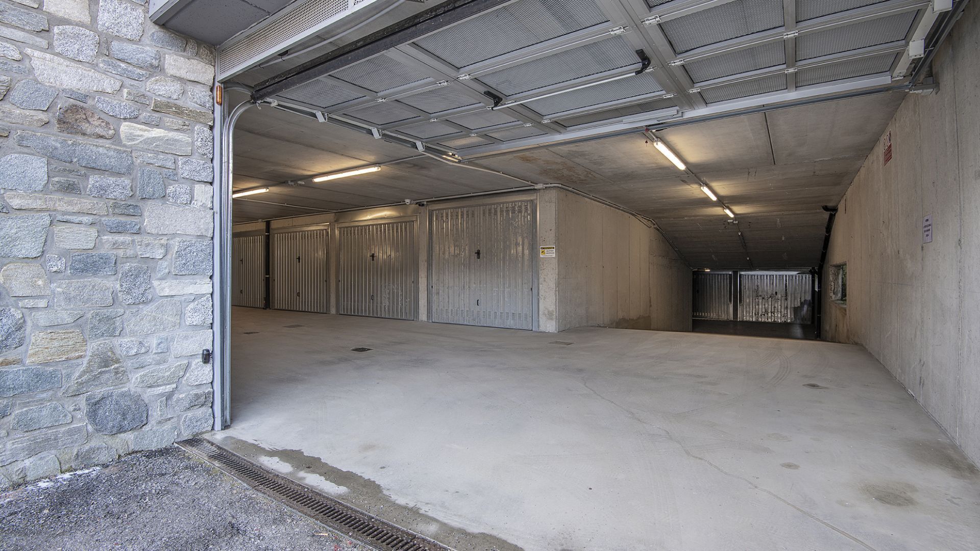 A spacious, industrial-style garage with concrete floors and metal doors, featuring a stone wall on one side.
