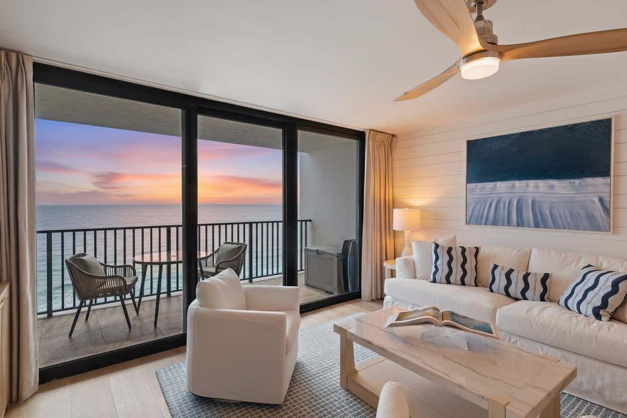 Une chambre d’hôtel moderne dotée d’un grand balcon, d’un canapé blanc, d’une table basse et d’un tableau accroché au mur.
