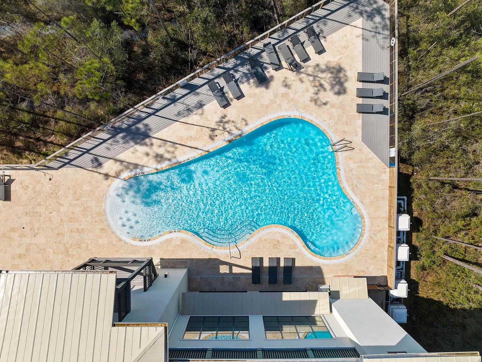An aerial view of a swimming pool with a deck and lounge chairs, surrounded by trees.
