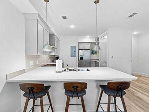 A modern kitchen with a large island, bar stools, stainless steel appliances, and pendant lighting. - 30A Hideaway | Pool, Gym & Near Beaches (Santa Rosa Beach)