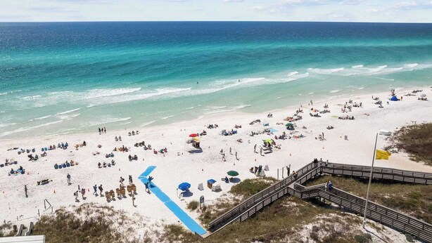 Una spiaggia con una passerella di legno che conduce all'acqua, e una vista limpida sull'oceano.
