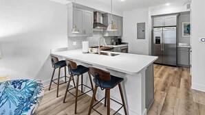 Una cucina moderna con isola centrale, sgabelli da bar, elettrodomestici in acciaio inossidabile e illuminazione a sospensione.
