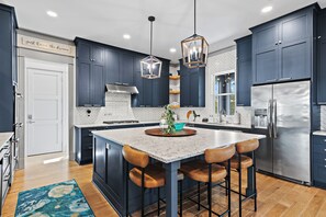 A modern kitchen with dark blue cabinets, a large island with bar stools, stainless steel appliances, and pendant lighting. - Luxury Lakefront w/ Dock + Gourmet Kitchen (Santa Rosa Beach)