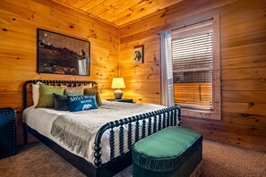 A wooden-paneled bedroom with a bed, pillows, a nightstand, a lamp, and a window with blinds. - Mistwood Manor | Hot Tub • Sauna • Game Room (Sevierville)