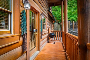 A wooden cabin with a covered porch, a stone wall, and a metal grill. - Mistwood Manor | Mtn Views • Hot Tub • Game Room (Sevierville)