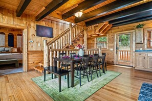 A wooden cabin interior with a dining area, staircase, and a television mounted on the wall. - Mistwood Manor | Hot Tub • Sauna • Game Room (Sevierville)