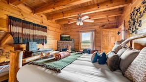 Interno di una baita di legno con un letto, una televisione, un caminetto e una ventola a soffitto.