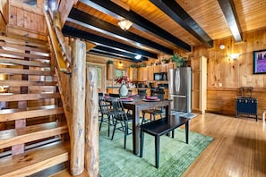 A wooden interior with a staircase, a dining area with chairs and a table, and a kitchen with appliances. - Mistwood Manor | Mtn Views • Hot Tub • Game Room (Sevierville)