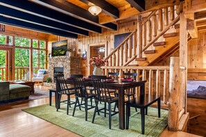 Ein Holzinterieur mit Kamin aus Stein, einem Essbereich mit Stühlen und einer Treppe.