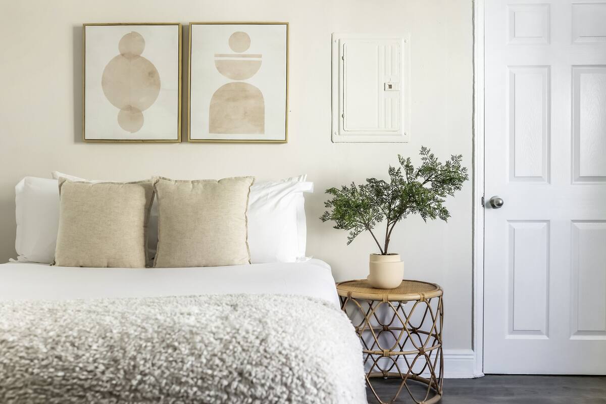 A bedroom with a bed, two framed abstract paintings, a potted plant, and a white door.