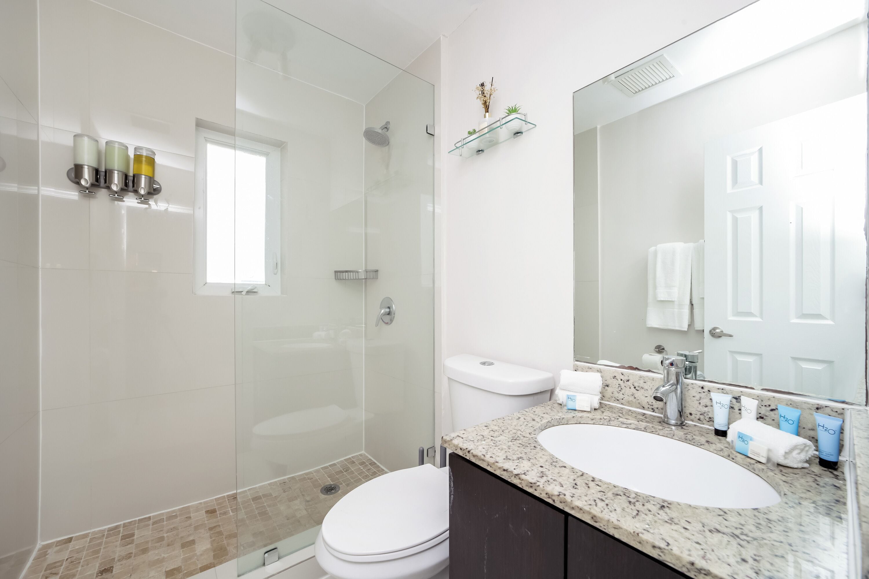 Une salle de bain moderne avec une douche à parois de verre, des toilettes blanches, un lavabo avec un plan de travail en granit et un miroir au-dessus du lavabo.