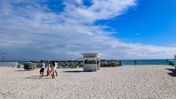 A beach with a lifeguard tower, beach chairs, umbrellas, and a clear sky. - The Donovan Hotel (Miami Beach)