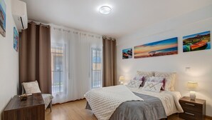 A bedroom with a bed, bedside tables, a chair, a desk, and curtains. - ‘Ria Formosa Pool Heaven’ Apartment with Shared Pool, Wi-Fi, and Air Conditioning (Olhão)
