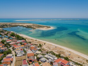 An aerial view of a coastal town with houses, a beach, and clear blue waters. - ‘Ria Formosa Pool Heaven’ Apartment with Shared Pool, Wi-Fi, and Air Conditioning (Olhão)