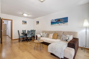 A living room with a sofa, a dining table with chairs, a lamp, and artwork on the walls. - Apartment 'Ria Formosa Pool Haven' with Shared Pool, Wi-Fi and Air Conditioning (Olhão)