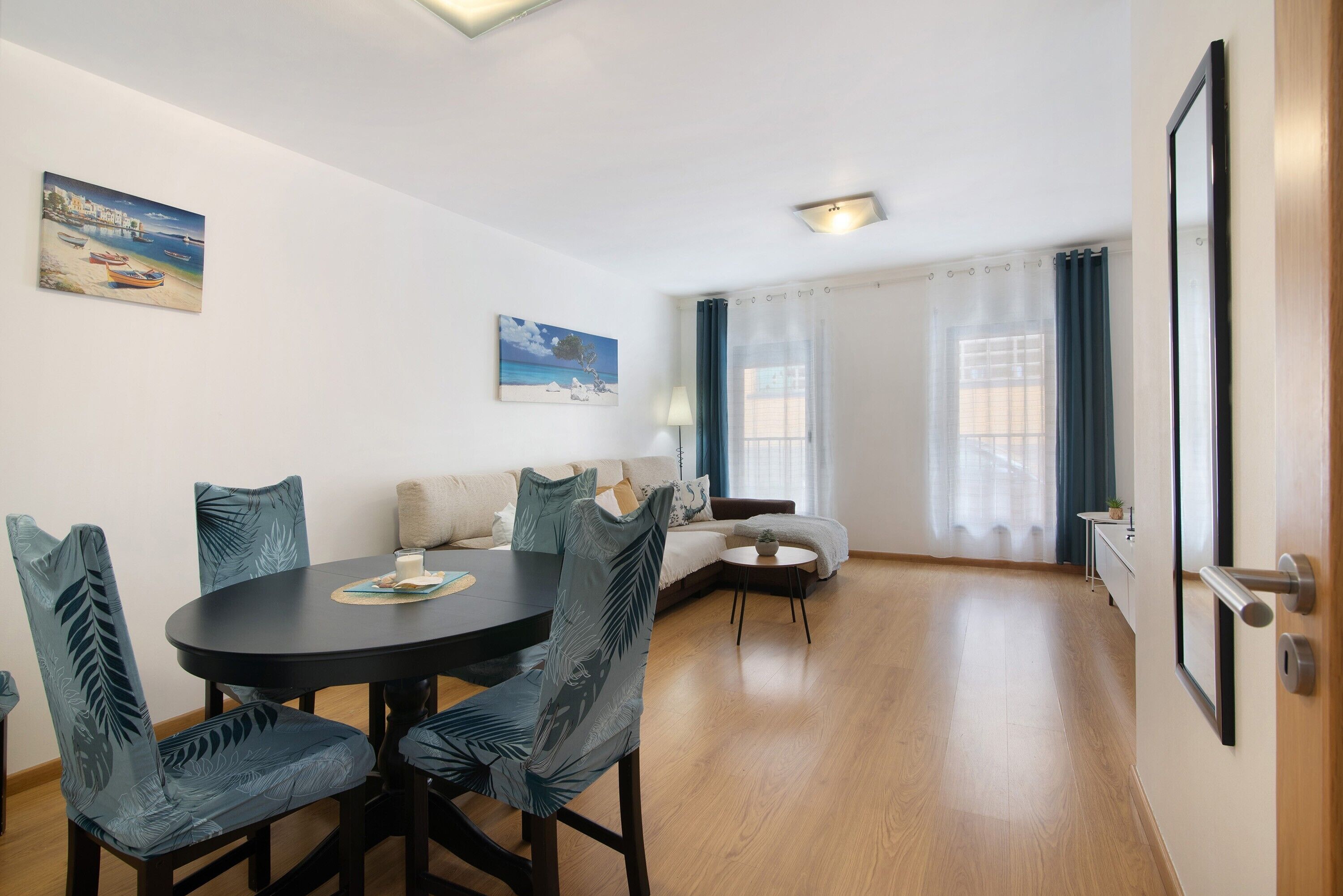 A dining area with a round table and chairs, a sofa, and a painting on the wall.