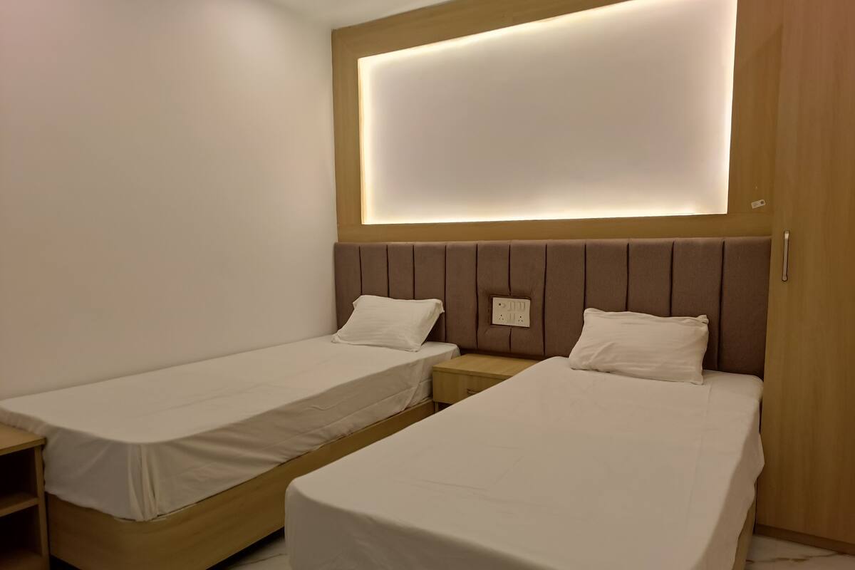 A hotel room with two single beds, a wooden headboard, a bedside table, and a wall-mounted light fixture.