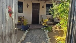 A pathway leading to a building with a brown door, surrounded by potted plants and a wooden fence. - Charming Private Cottage in Tranquil San Pedrito, El Pescadero- 2 Blocks to Surf (El Pescadero)